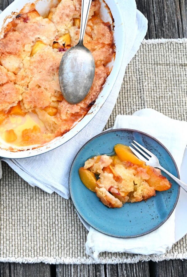 Peach Cobbler in in einer Auflaufform, vorne 1 Stück auf blauem Teller