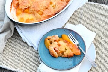 Peach Cobbler in in einer Auflaufform, vorne 1 Stück auf blauem Teller