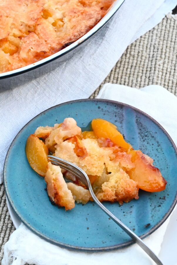 Peach Cobbler, Pfirsichkuchen in einer Auflaufform, 1 Stück auf blauem Teller, mit Gabel drin