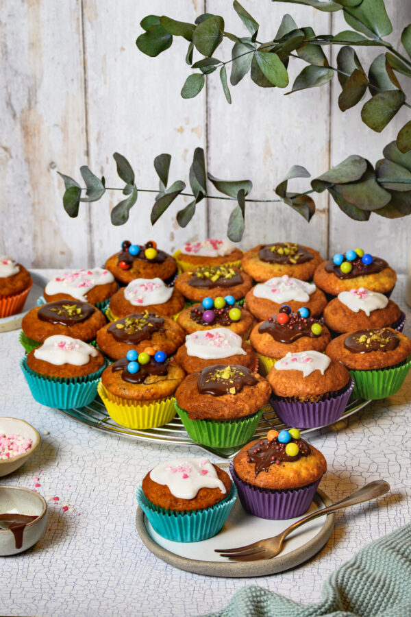 Viele Muffins mit unterschiedlicher Deko auf rundem Backgitter, von schräg vorne