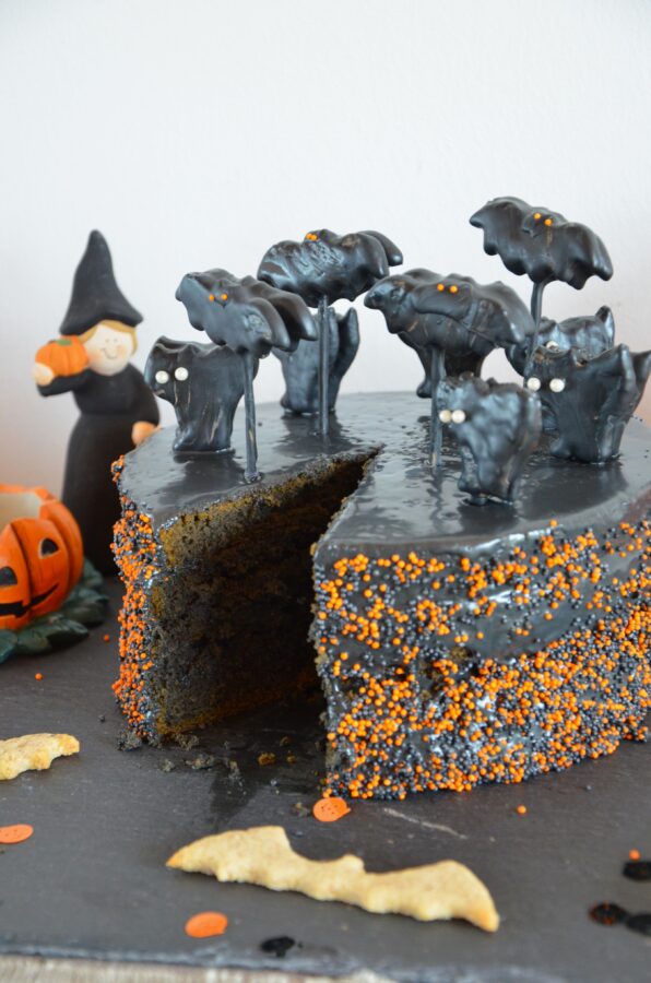 Schwarzgraue Halloween-Torte mit Katzen- und Fledermaus-Deko, angeschnitten, auf schwarzem Untergrund