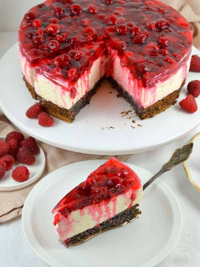 Himbeertorte mit Topfencreme und Mohnboden  auf weißer Tortenplatte, davor 1 Stück auf einem Teller