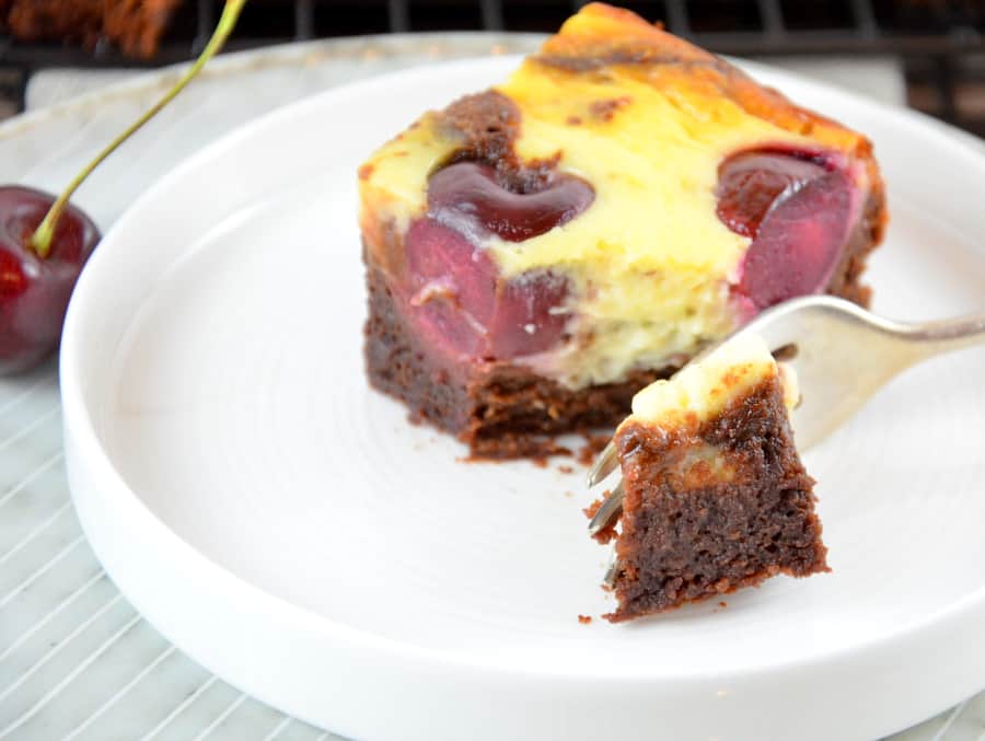 Cheesecake Brownies mit Kirschen, ein Stück auf Teller, Gabel teilt einen Bissen ab