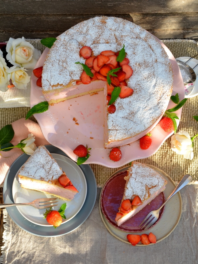 Erdbeer-Käsesahne-Torte von oben, zwei Stück auf Tellern, hinten die Torte