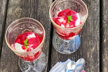 2 Gläser Himbeer-Mascarpone-Dessert, auf grauen Holzbrettern, von schräg vorne