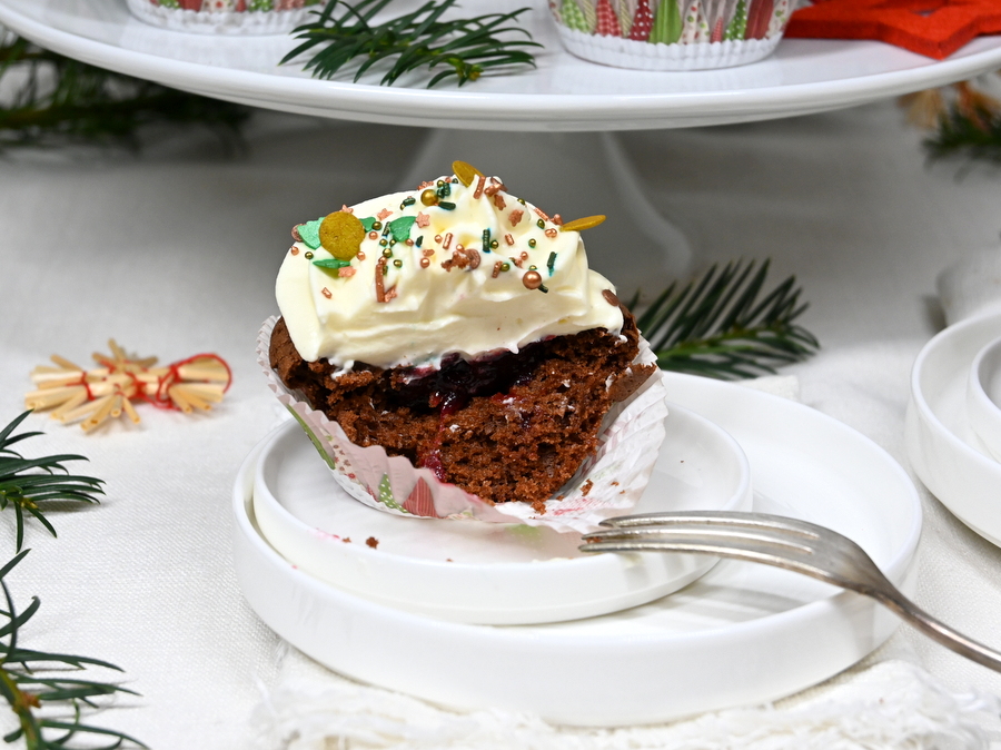 Weihnachtliche Schoko-Cupcakes mit Frischkäse Topping: 1 Cupcake an Teller, halb aufgegessen, Blick auf die Preislebeerfülle