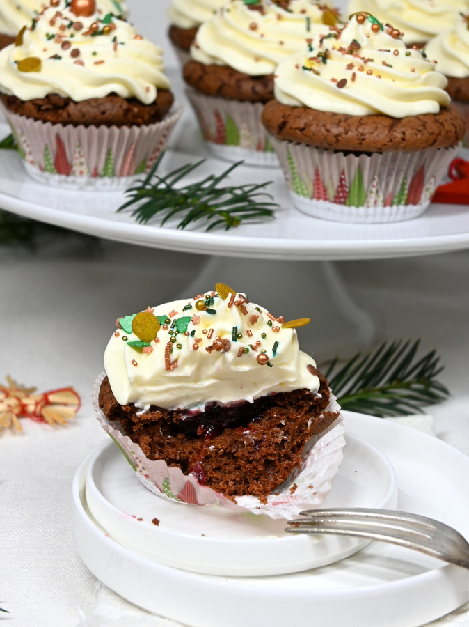 Weihnachtliche Schoko-Cupcakes mit Frischkäse Topping: 1 Cupcake an Teller, halb aufgegessen, Blick auf die Preislebeerfülle