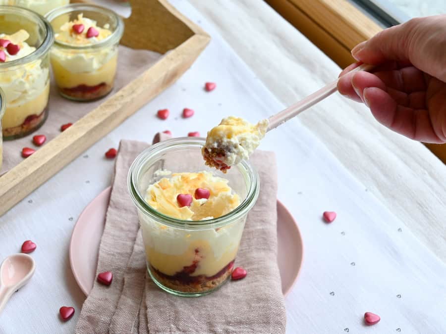 Kokos-Dessert mit Himbeermarmelade und roten Zuckerherzen im Glas, mit rosa Löffel drin