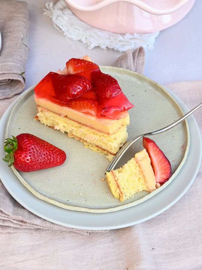 Erdbeertorte mit Vanillecreme, 1 Stück auf Teller, Gabel hat ein Stück davon abgestochen