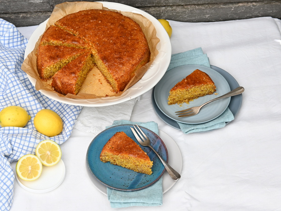 Zitronen-Polenta-Kuchen: 2 Stück vorne auf Tellern, hinten der Kuchen