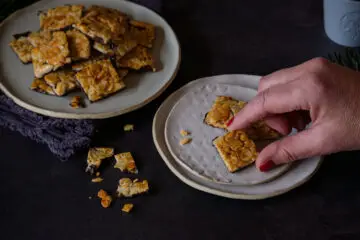 Florentiner mit Mandelblättchen und Karamell auf einem kleinen Teller, eine Hand greift nach einem Stück