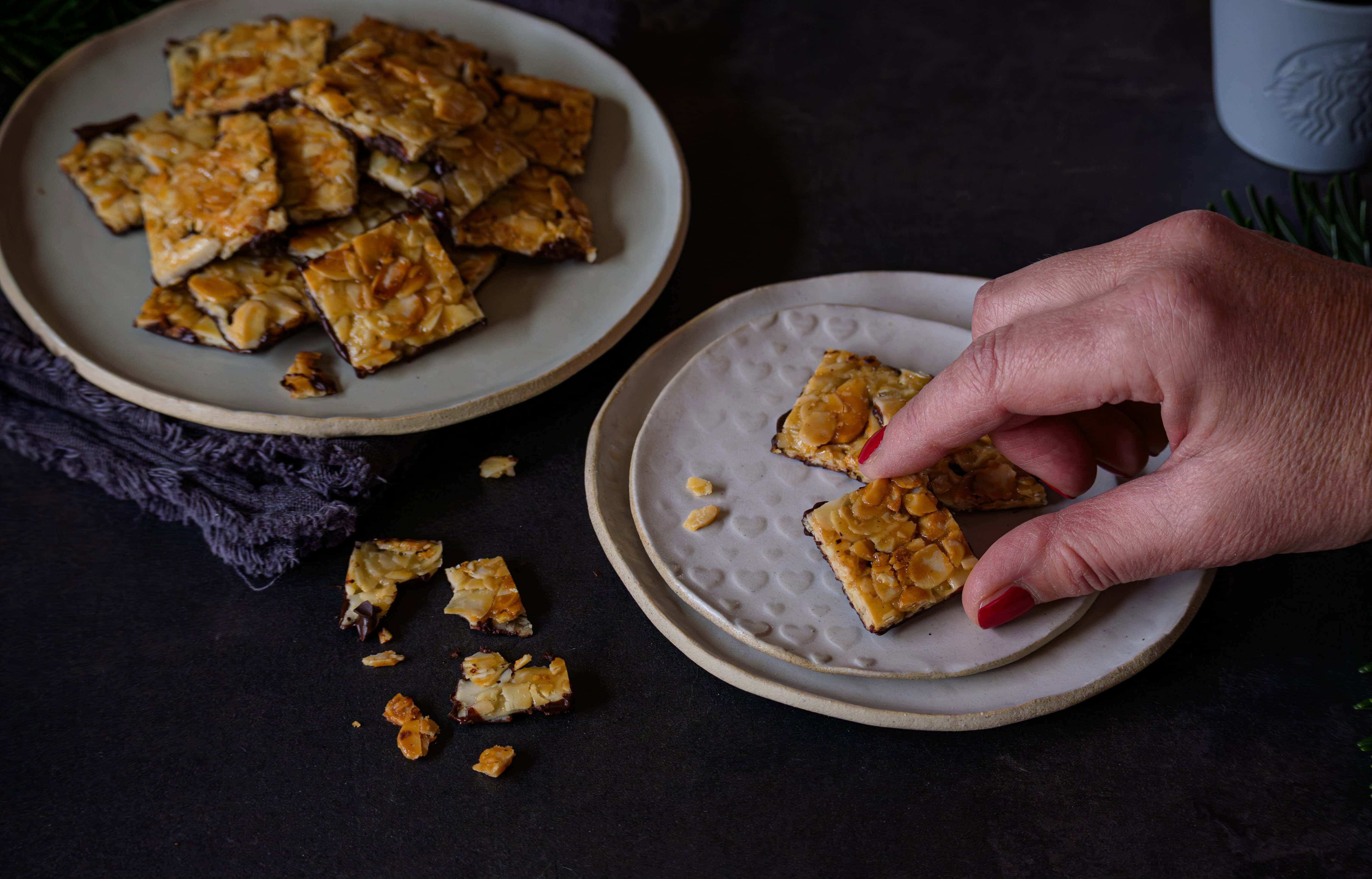 Florentiner mit Mandelblättchen und Karamell auf einem kleinen Teller, eine Hand greift nach einem Stück