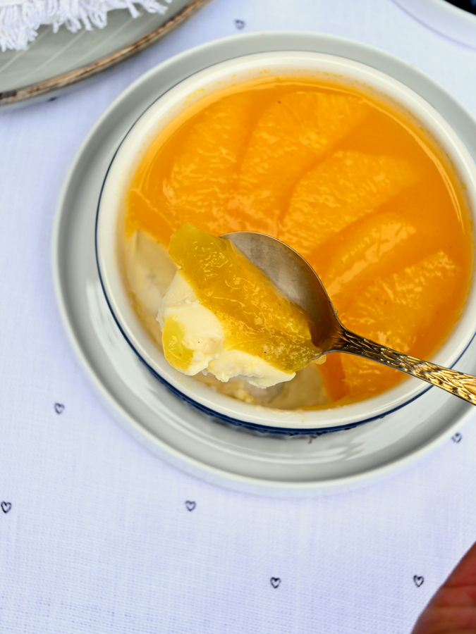 Panna Cotta mit Orangen, laktosefrei, ein Löffel hebt ein Stück heraus