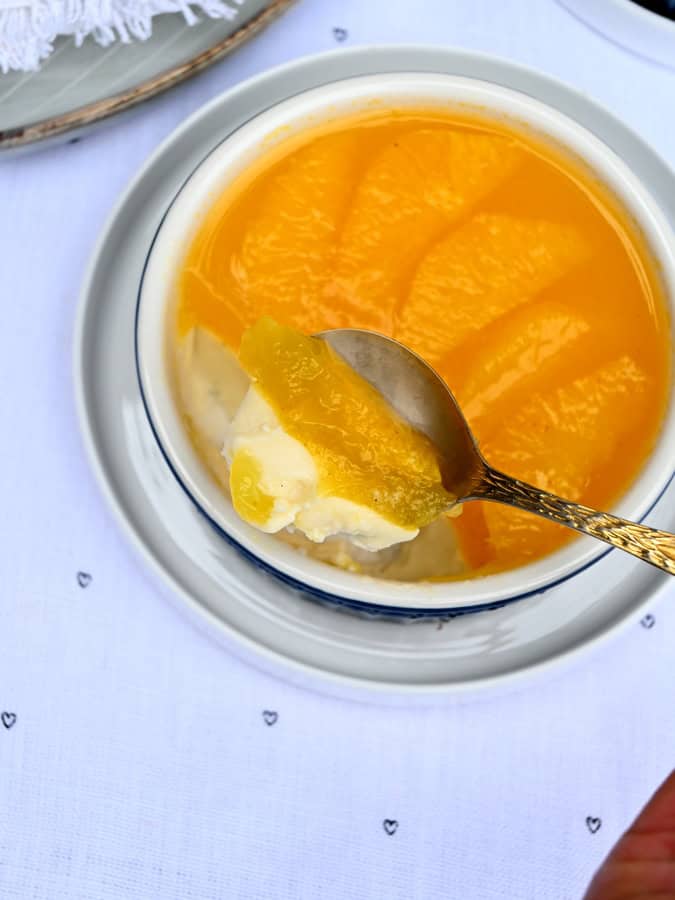 Panna Cotta mit Orangen in einer kleinen Schale, ein Löffel hebt ein Stück heraus