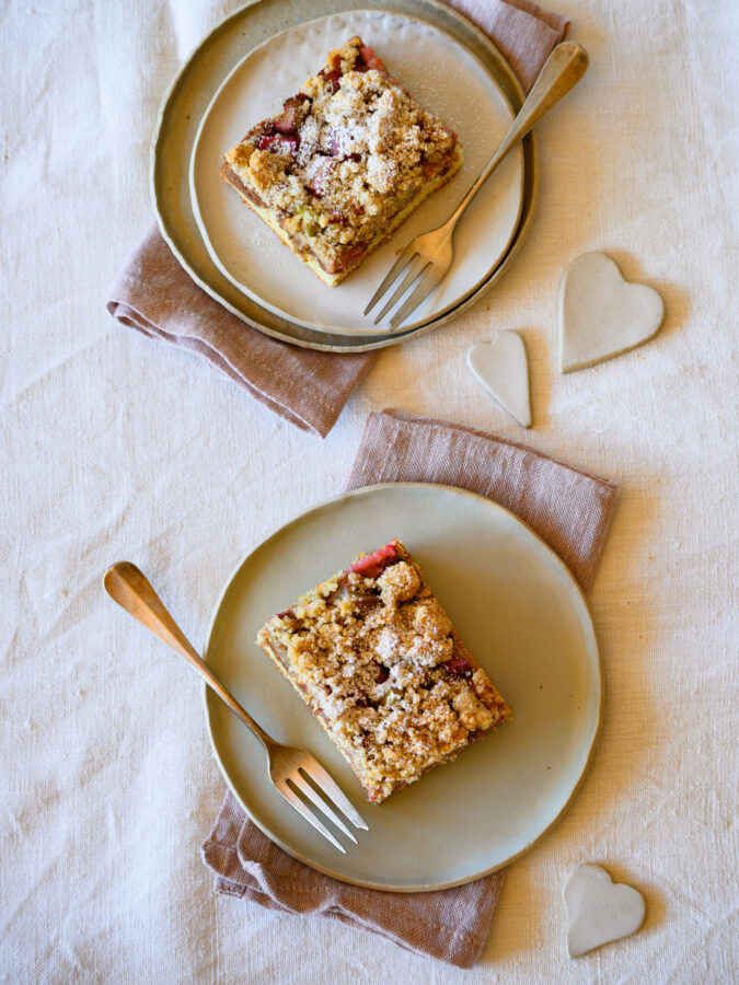 Rhabarberkuchen mit Mandelstreuseln, 2 Stück auf Tellern, hintereinander platziert, von oben