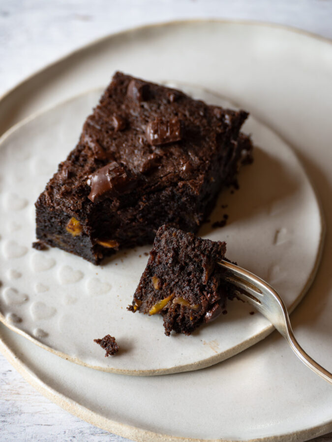 1 Zucchini-Brownie auf einem Teller, Gabel sticht ein Stück ab