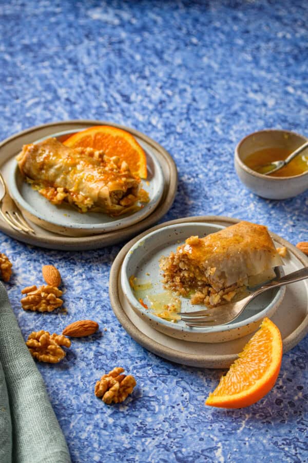 Selbstgemachte Baklava, 2 Stück auf Tellern, eines schon angeknabbert, von schräg vorne