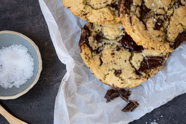 3 Stück vegane Chocolate Chip Cookies auf weißem Papier, auf einem schwarzen Untergrund, von oben