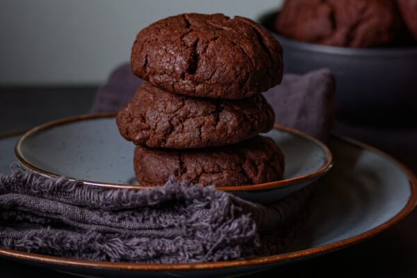 3 Chocolate Cookies mit Tahini gestapelt auf blauem Teller, Dark & Moody, von vorne