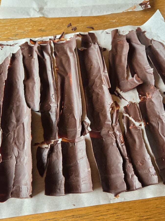 Selbstgemachtes Schokoladendekor: dünne längliche Schokospiltter auf Backpapier