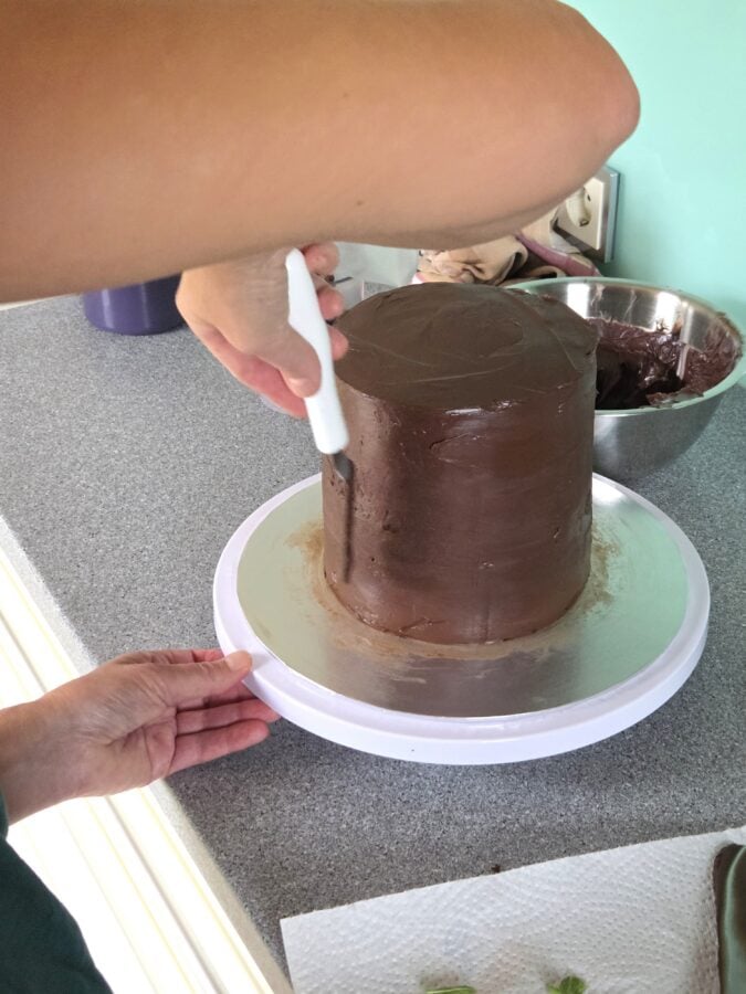 Bei einer hohen Schokoladentorte wird der Tortenrand mit Schokoladenganache eingestrichen
