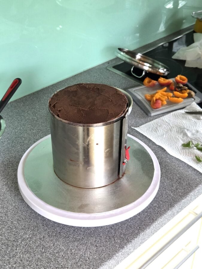 Eine hohe geschichtete Schokoladentorte auf einem drehbarem Tortenteller, eingespannt in einen Tortenring