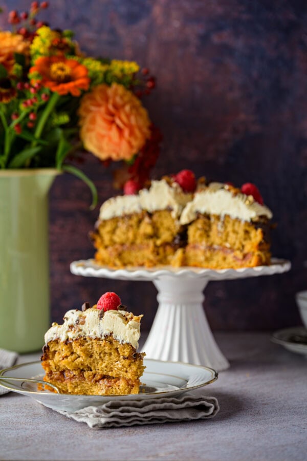 Kaffeebuttercremetorte mit Pekan-Salzkaramell auf einer weißen Tortenplatte, vorne 1 Stück auf einem Teller, im Hintergrund ein bunter Blumenstrauß