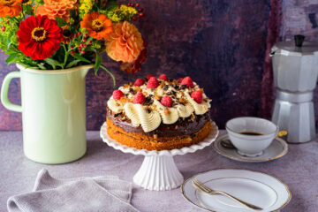 Kaffeebuttercremetorte mit Pekan-Salzkaramell auf einer weißen Tortenplatte, von schräg vorne, hinten ein bunter Blumenstrauß