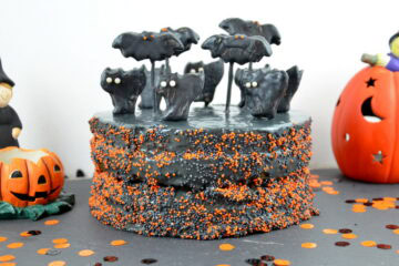 Dunkelgrau-schwarze Halloween-Torte mit einer Deko aus schwarzen Katzen- und Fledermaus-Keksen