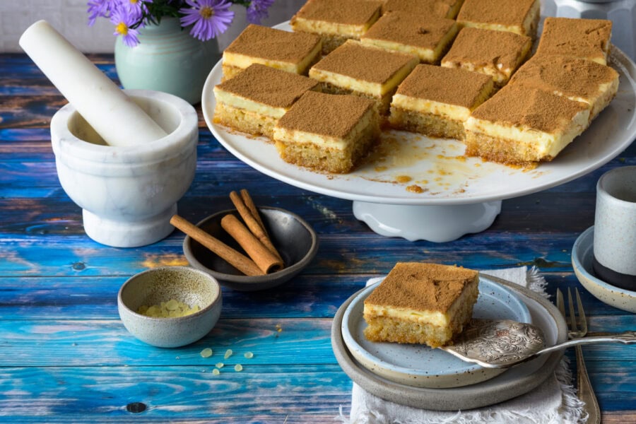 Politiko Dessert: Griechischer Grießkuchen mit Zimt in quadratische Stücke geschnitten auf Tortenplatte und Teller, von schräg vorne