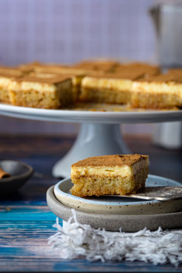 Politiko Dessert, griechischer Grießkuchen mit Zimt: vorne ein Stück auf einem Teller, hinten weitere Stück auf einer Tortenplatte