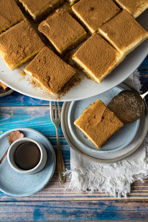 Politiko Dessert: Griechischer Grießkuchen mit Zimt in quadratische Stücke geschnitten auf Tortenplatte und Teller, von oben