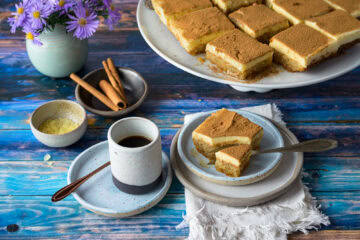 Politiko Dessert: Griechischer Grießkuchen mit Zimt: ein Stück auf einem Teller, mit Gabel drin, von schräg vorne, hinten weitere Stück auf einer Tortenplatte